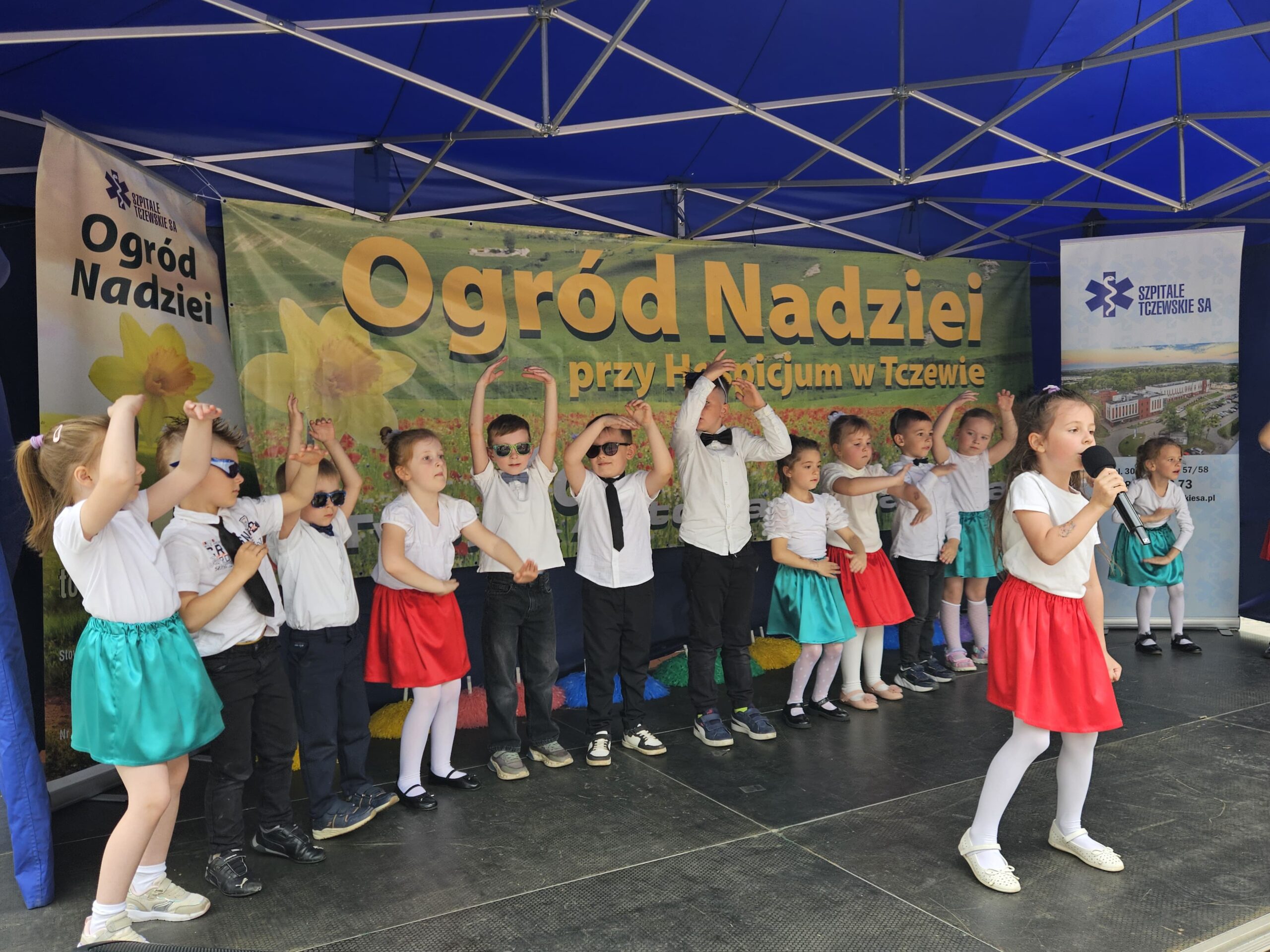 Dziewczynka śpiewa do mikrofonu, dzieci za nią tańczą