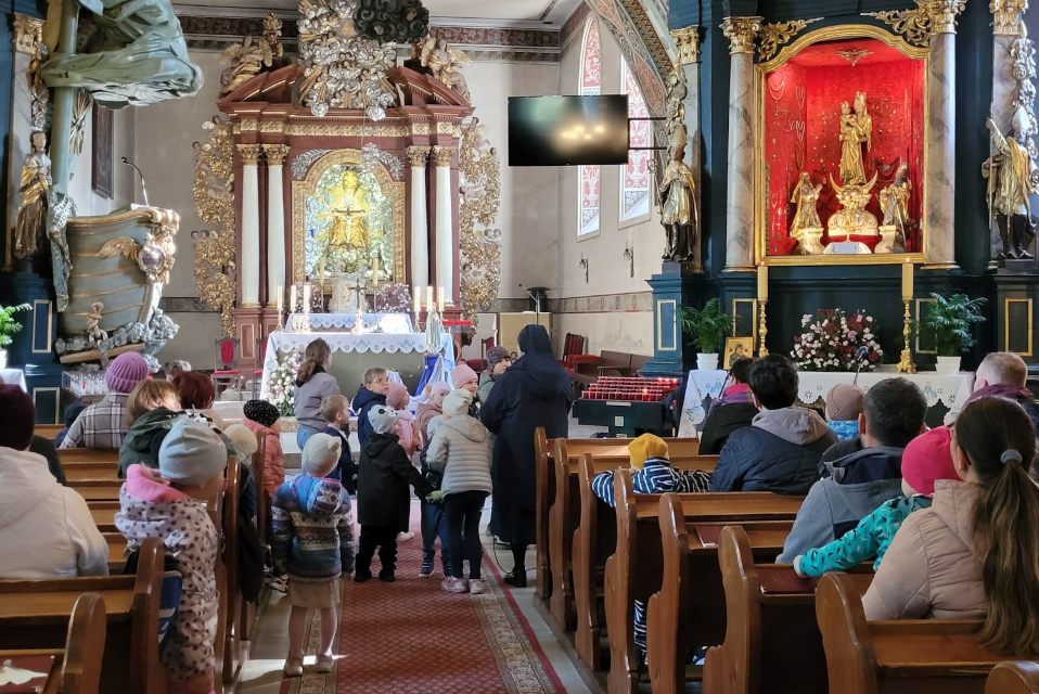 Wnetrze Sanktuarium Matki Bożej Pocieszenia w Lubiszewie. Ludzie siedzący w ławkach, dzieci stojące na środku kościoła wraz z siostrą