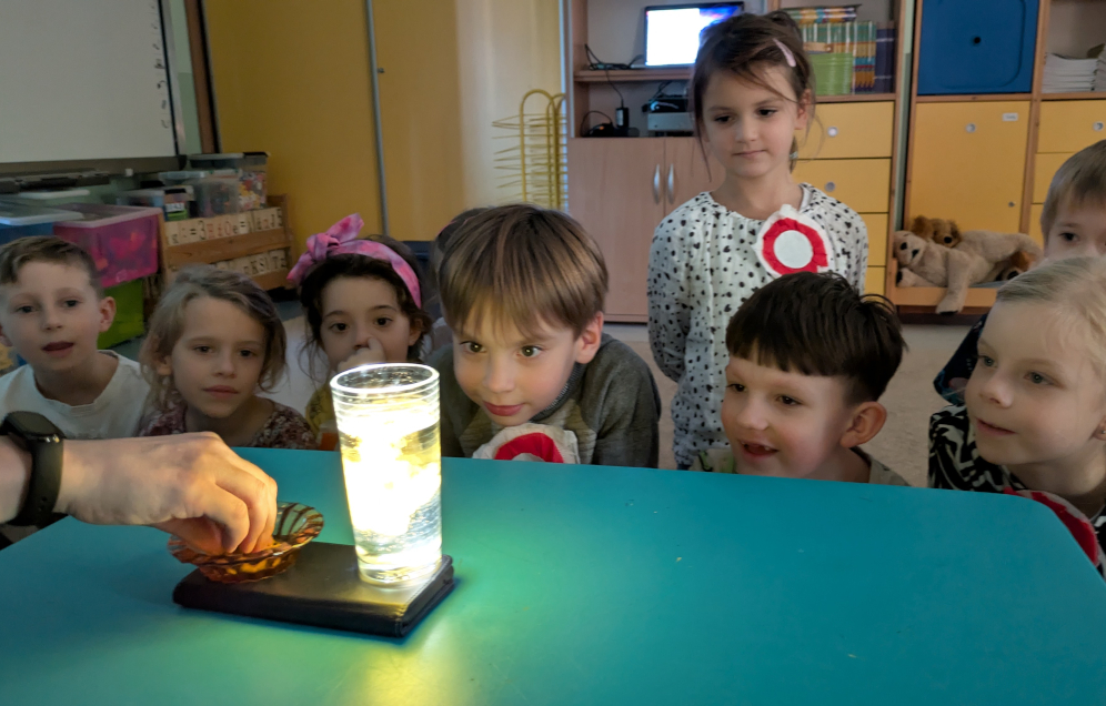 Dzieci patrzące z zaskoczeniem na świecącą wodę w szklance