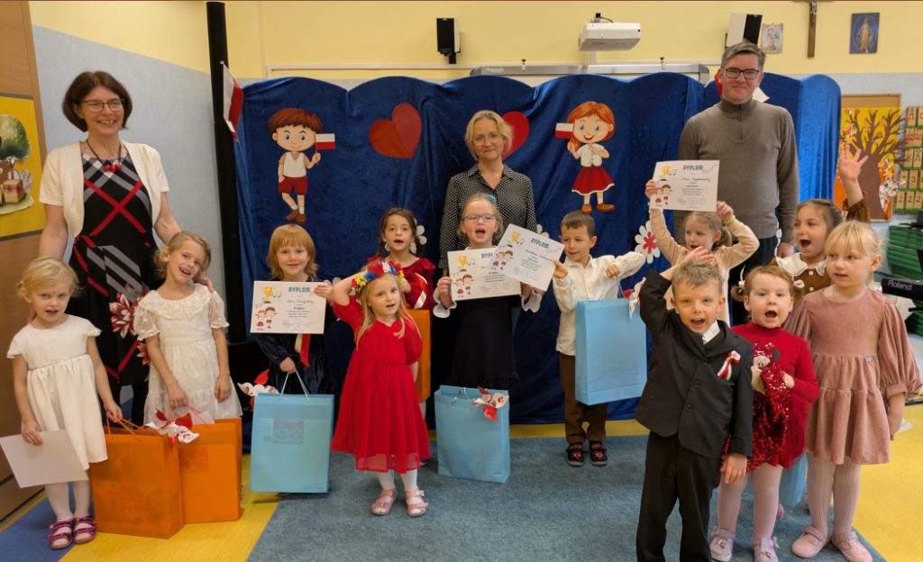 Uczestnicy konkursu piosenki patriotycznej pokazują dyplomu, za nimi stoi komisja konkursowa