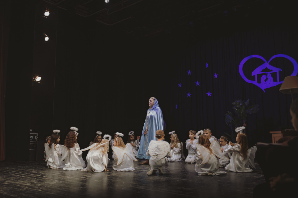 Na środku sceny Maryja, wokół niej klęczące dzieci przebrane za anioły