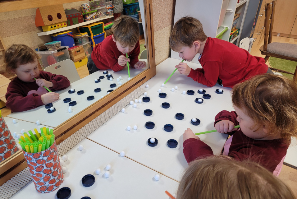 Dzieci trzymają słomkę ustami i przenoszą styropianowe kulki na zakrętkę