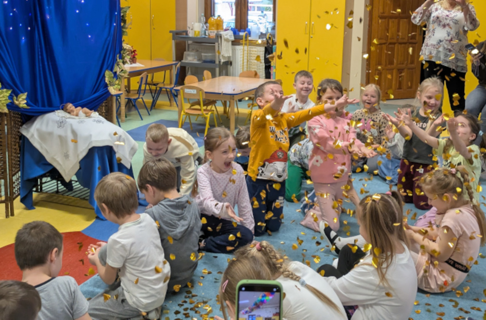 Dzieci siedzące na dywanie i zbierające fruwające w powietrzu konfetti