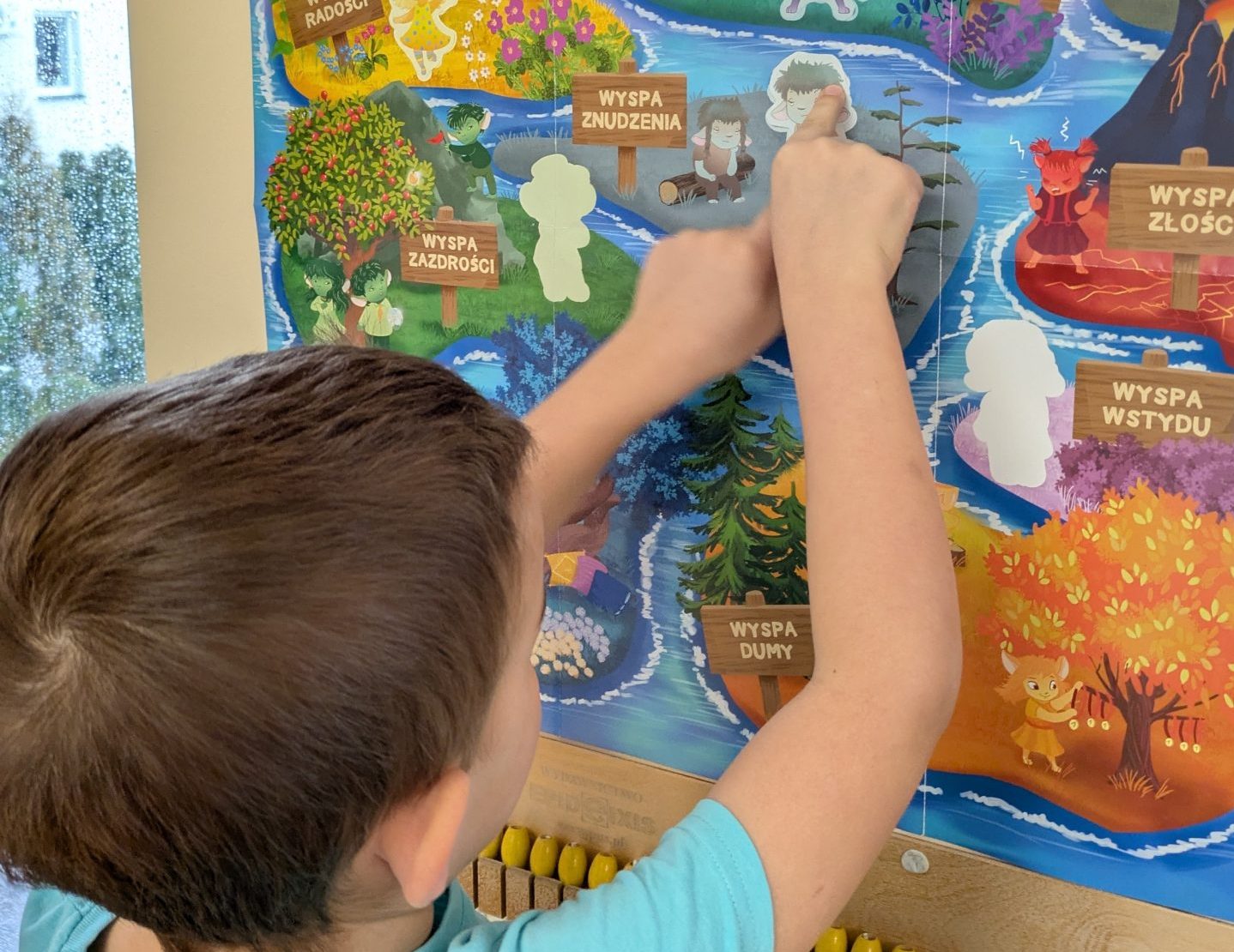 chłopiec przykleja sylwetę kolejnego bohatera projektu Czuciaki na plakacie
