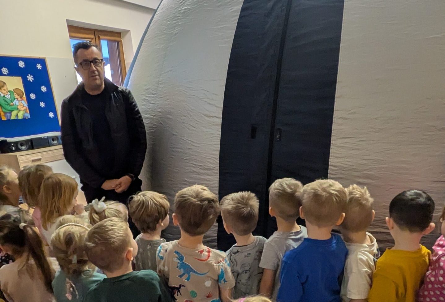 Dzieci stoją przed wejściem do kina sferycznego, pan opowiada dzieciom o kinie