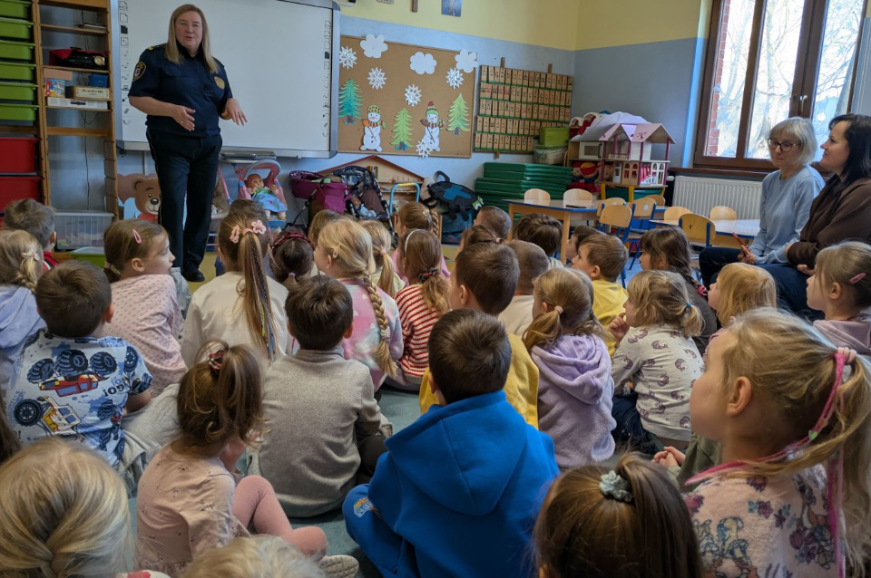 Strażnik Miejski stoi przed grupą dzieci i opowiada, dzieci słuchają