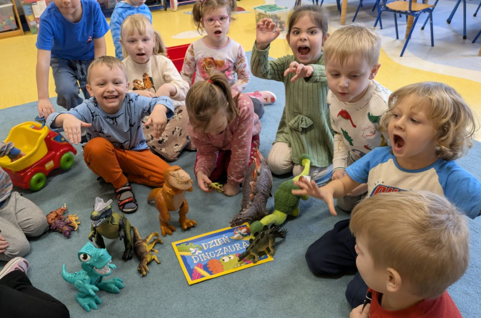 Dzieci udają dinozaury - pokazują to mimiką i gestem, na dywanie leżą zabawkowe dinozaury