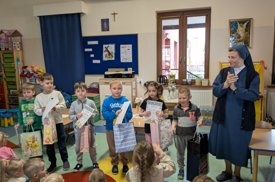 Dzieci stojące w rzędzie z dyplomami i upominkami, Siostra Dyrektor klaszcze w dłonie i uśmiecha się do dzieci