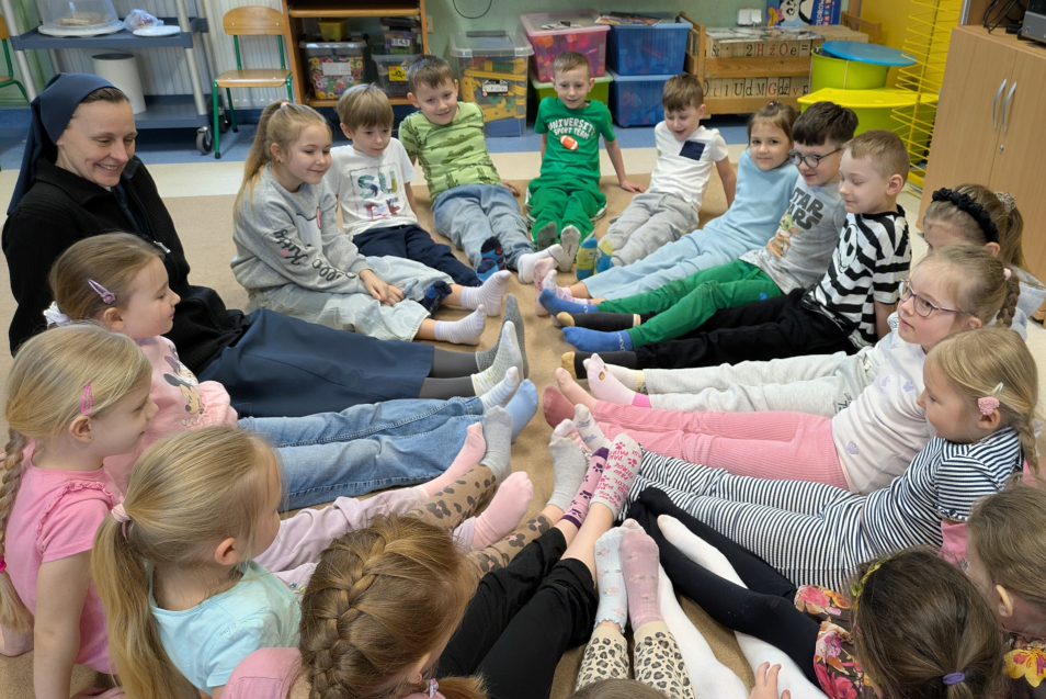 Dzieci wraz z siostrą siedzą w kole, mają wyciągnięte nogi do środka koła i pokazują swoje kolorowe skarpetki nie do pary