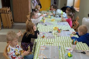 Dzieci siedzą przy stole i ozdabiają papierowy liść