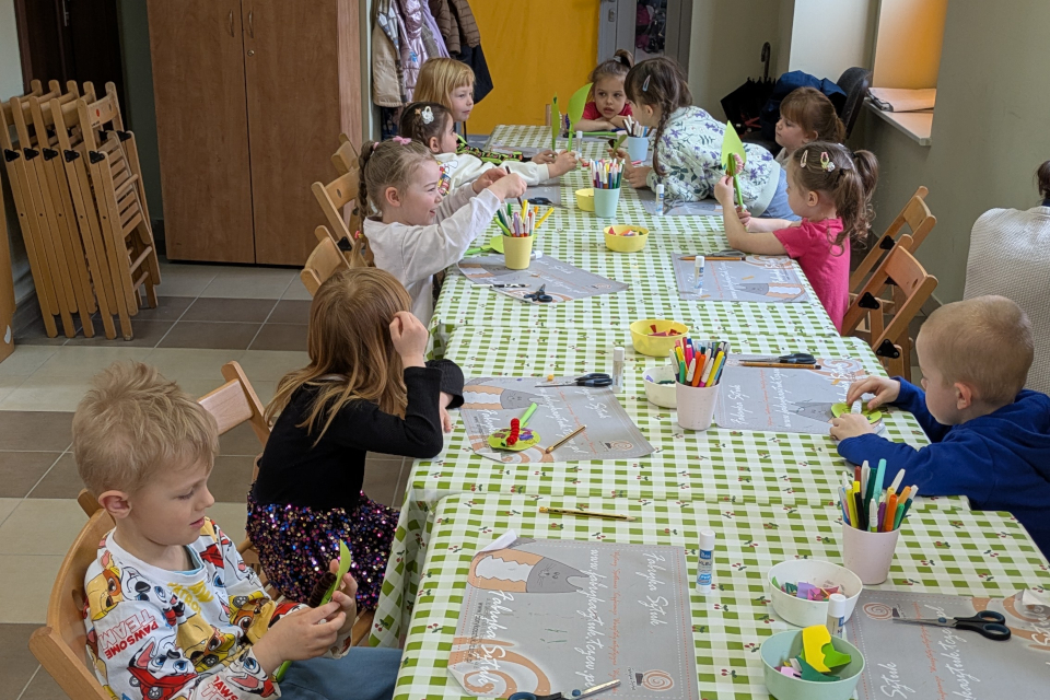 Dzieci siedzą przy stole i ozdabiają papierowy liść