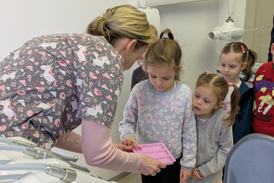 Pani stomatolog pokazuje dzieciom tackę z narzędziami stomatologicznymi, Dzieci z zaciekawieniem patrzą na tacę