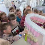 Chłopiec myje wielką sztuczną szczękę dużą szczoteczką, inne dzieci patrzą