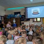 Przedszkolaki siedzą i patrzą na ekran na którym jest tort