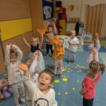 Dzieci pokazujące pomarańczowe kółka z papieru zebrane dywanu, na którym są koła w różnych kolorach