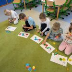 Dzieci układające koła na kartce, na której narysowana jest głowa gąsienicy