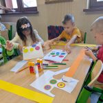 Dzieci siedzą przy stolikach i wycinają koła z papieru