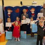 Uczestnicy konkursu piosenki patriotycznej pokazują dyplomu, za nimi stoi komisja konkursowa