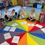 dzieci siedzą na chuście z ilustracjami świętych