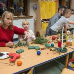 Dziewczynka z mamą robią stroik świąteczny, po prawej stronie inna rodzina