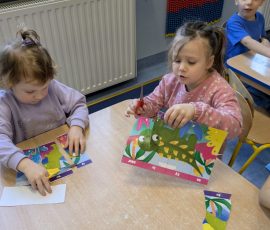 dziewczynki wycinają elementy pracy plastycznej w dinozaurem